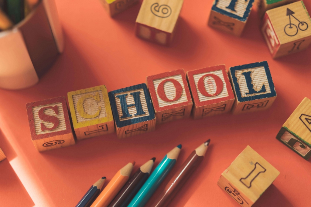 Wooden alphabet blocks spelling SCHOOL with colored pencils on an orange background