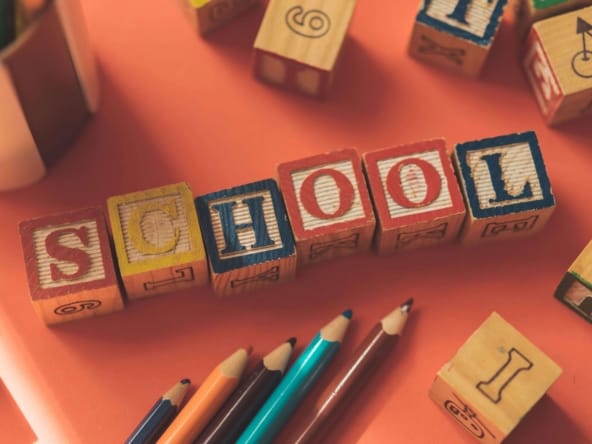 Wooden alphabet blocks spelling SCHOOL with colored pencils on an orange background